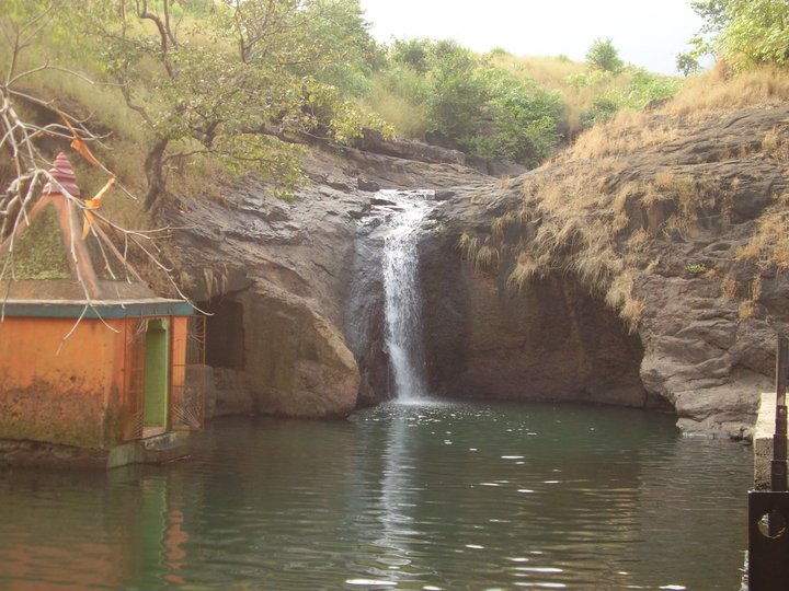 Kondeshwar waterfall beside a small temple in a rocky forest setting